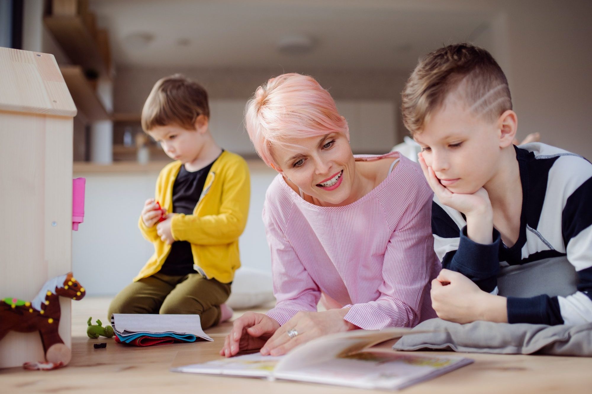 a-young-woman-with-two-children-reading-book-and-playing-on-the-floor–e1619662218134.jpg